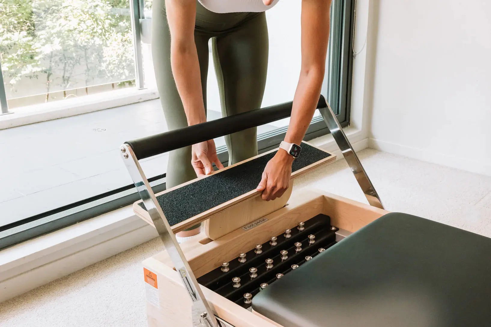 A person removing the carriage extender of a wooden Pilates reformer to see the springs.