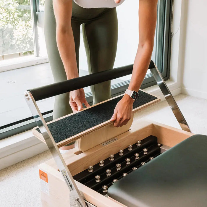 A person removing the carriage extender of a wooden Pilates reformer to see the springs.