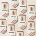 Multiple pairs of white and brown socks with 'elliossa' branding and brown dog illustrations embroidered, with brown paw print grips on the sole over a beige background.