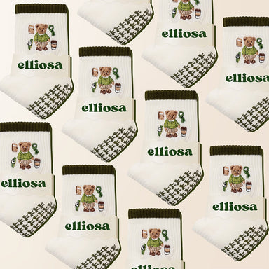 Multiple pairs of socks with teddy bear designs and 'elliosa' branding on a beige background.