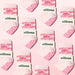Pattern of pink and white socks with 'elliosa' branding in the packaging on a pink background. The socks have pink heart shaped grips on the soles and the words 'pilates girl era' embroidered with hearts on the ankle.
