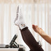 Person on a pilates reformer bed wearing white socks with brown coffee bean shaped grips on the soles, with coffee themed design on the ankle.