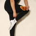 Person wearing black leggings and white socks with brown ruffles, coffee bean shaped grips on the soles and image of coffee and a croissant embroidered with the text 'pilates & lattes' on the ankle.