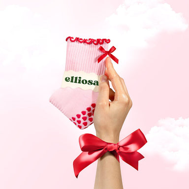Hand holding a pink sock with a red bow, featuring the brand 'elliosa'.