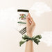 Hand holding a branded product with a bow, on a light background