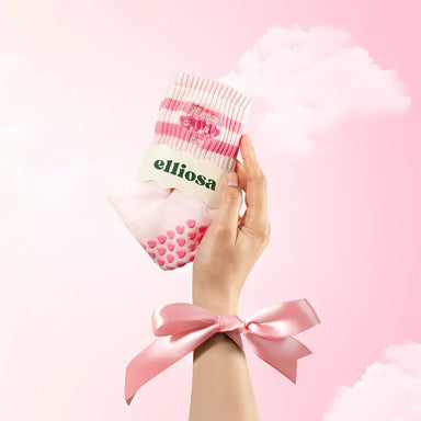 Hand holding a pink and white sock with 'elliosa' branding against a pink background.