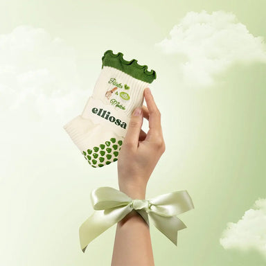 Hand holding a white sock with green accents and 'elliosa' branding against a light green background.