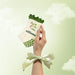 Hand holding a white sock with green accents and 'elliosa' branding against a light green background.