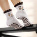 White socks with brown ruffles and an image of coffee and a croissant with the words "pilates & lattes" embroidered on the ankle, and coffee bean shaped grips on the soles. 