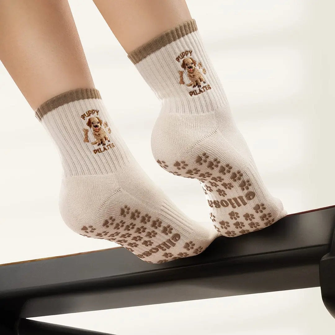 White socks with brown paw print grips on the sole and puppies and the words 'puppy pilates' embroidered. 