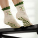 White socks with green heart shaped grips on the soles, with the text 'pilates & matcha' embroidered in green with images of matcha on the ankles.