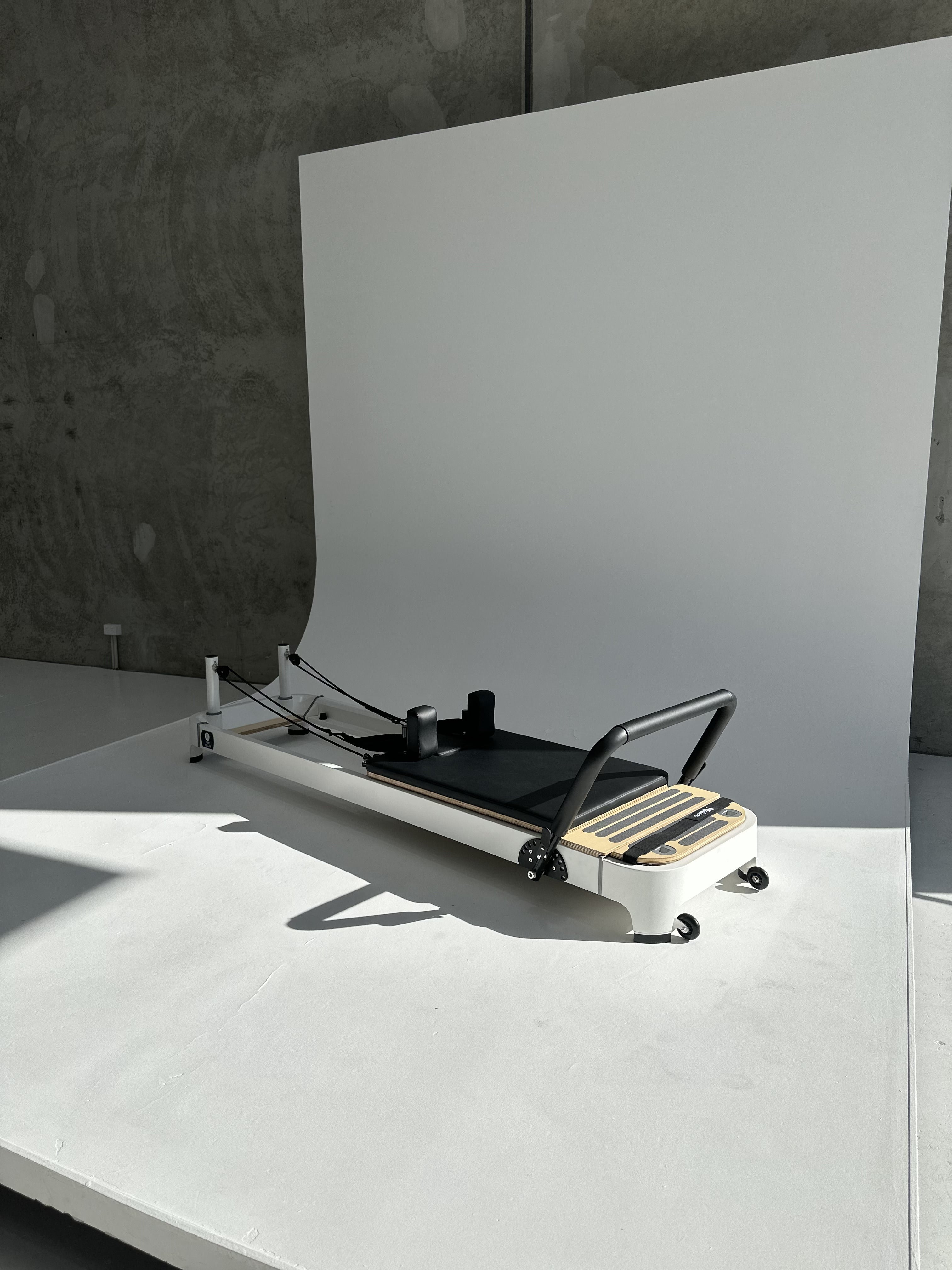 Core Collab Queen 2.0 Pilates reformer with white frame and black upholstery in a studio with white background.