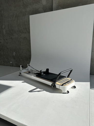 Core Collab Queen 2.0 Pilates reformer with white frame and black upholstery in a studio with white background.