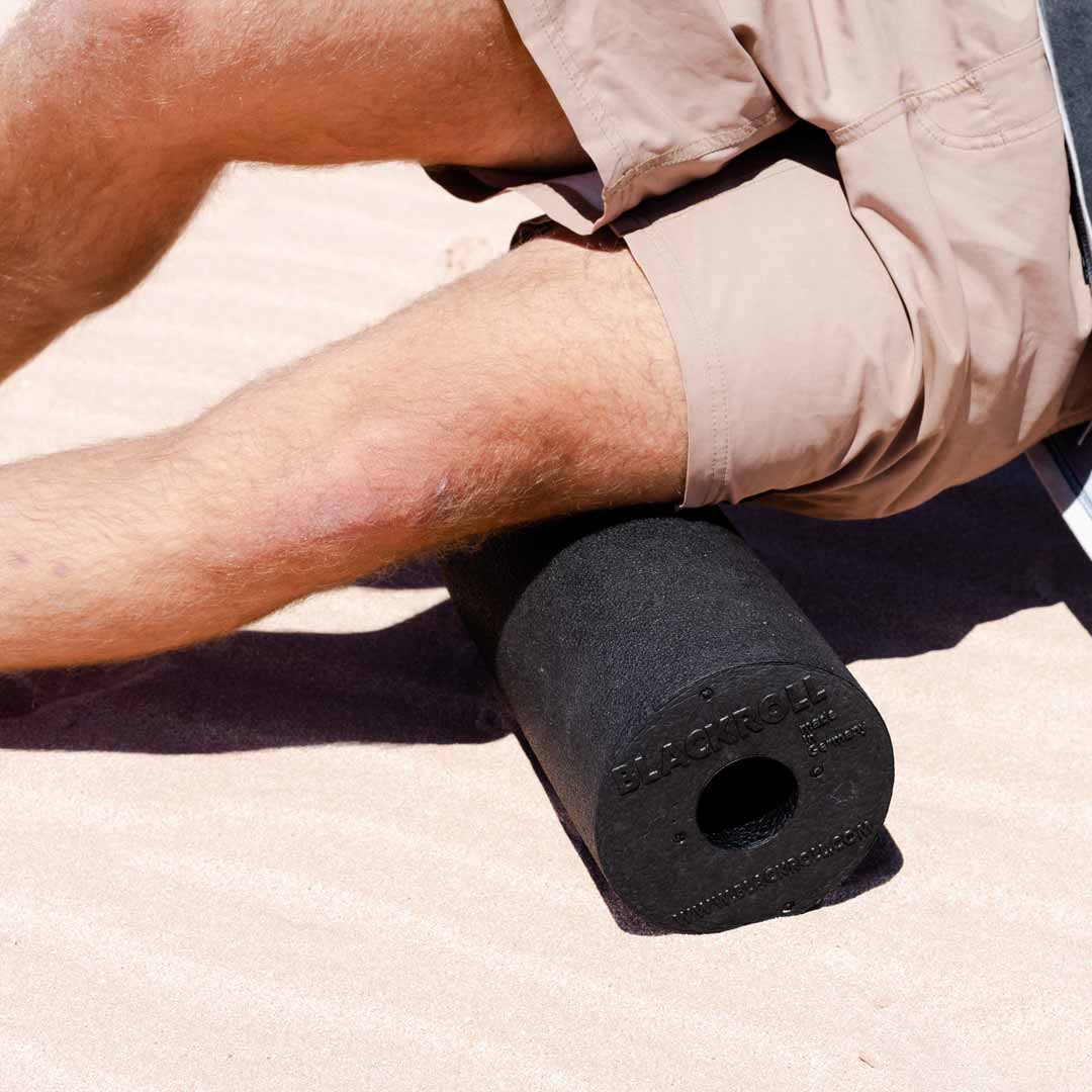 Person using black blackroll foam roller on the sand at the beach.