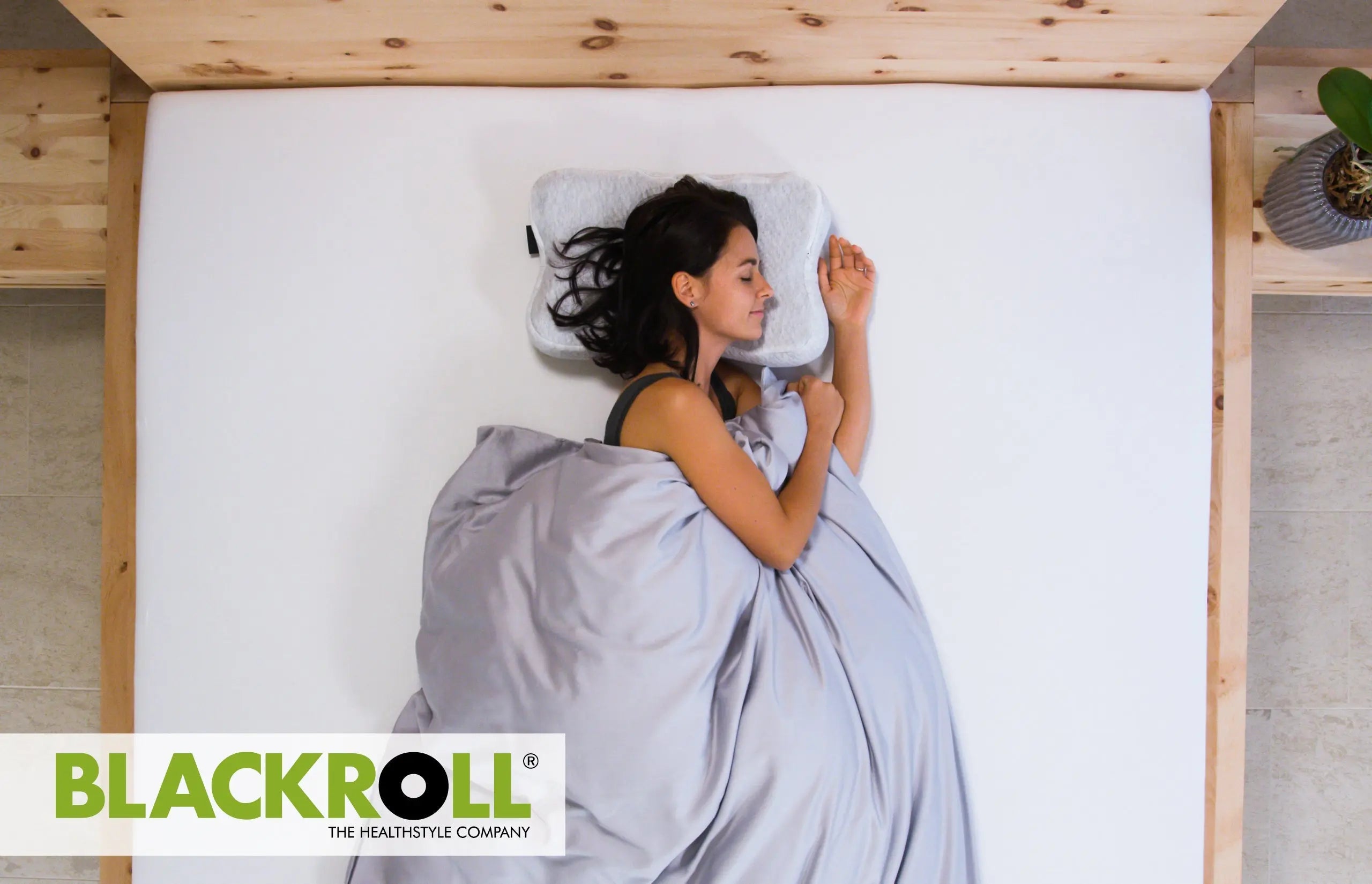 Woman sleeping on a bed using the Blackroll pillow with the brand logo visible.