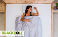 Woman sleeping in bed with a Blackroll recovery pillow, brand logo visible.