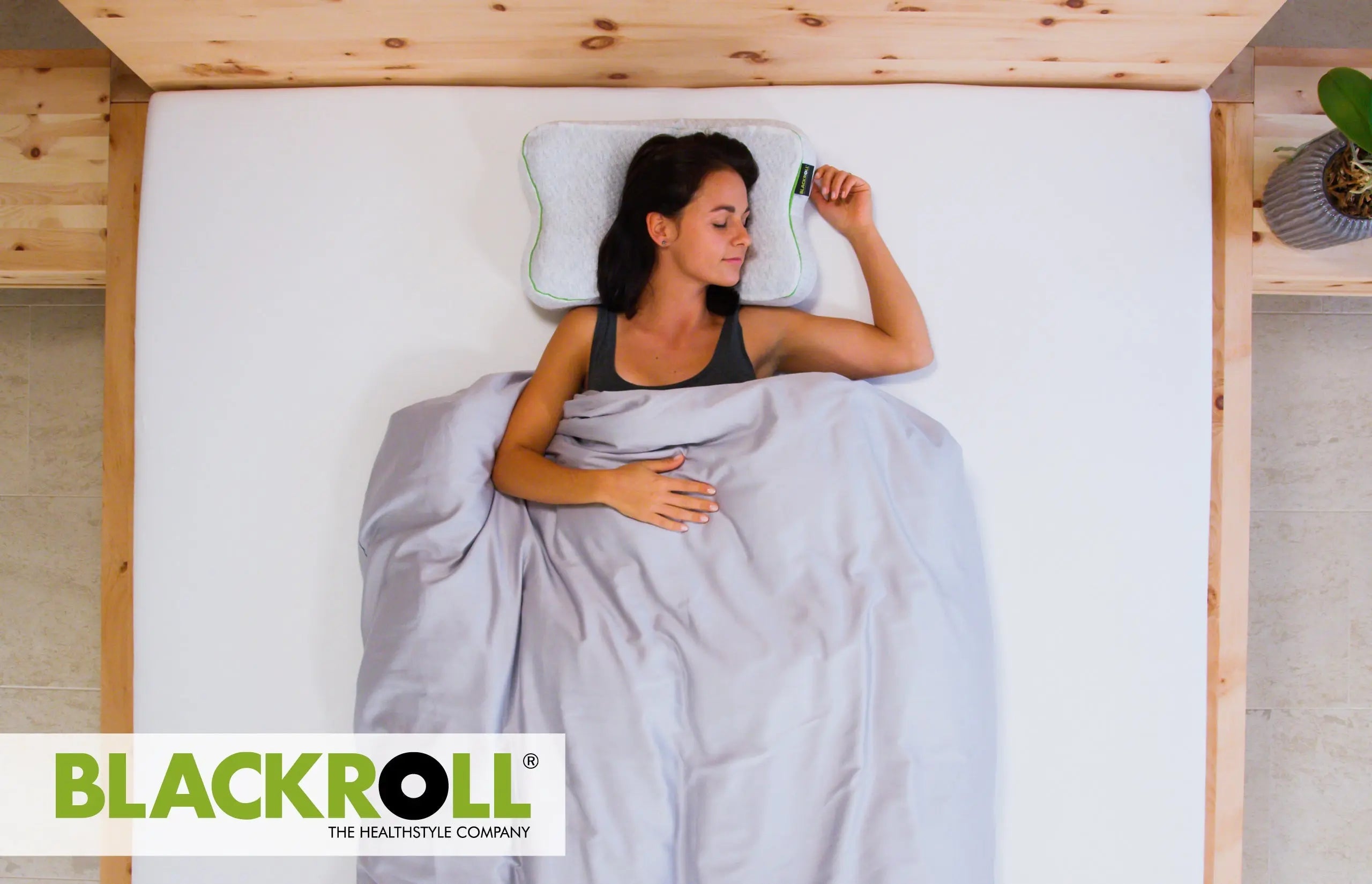 Woman sleeping in bed with a Blackroll recovery pillow, brand logo visible.