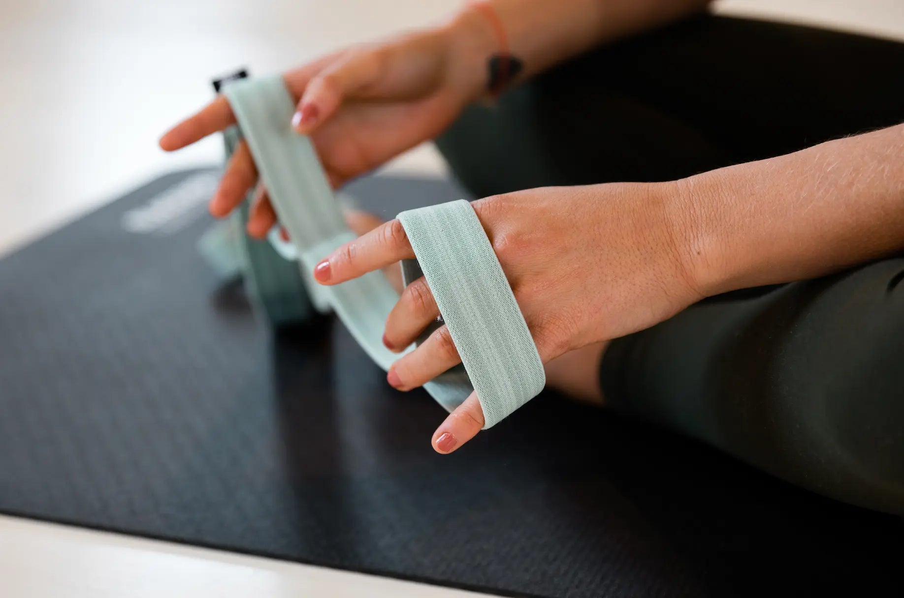 Close up of the hands of a person holding a Blackroll stretch band resistance band on a Pilates mat.