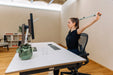 Person sitting at a desk and using the Blackroll stretch band to stretch her back and shoulders.