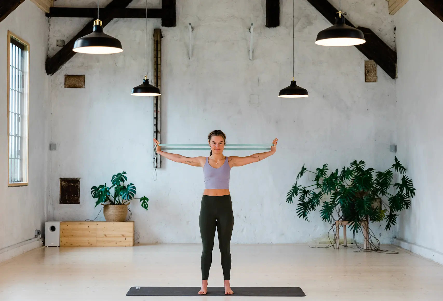 Woman using a Blackroll stretch band to stretch her shoulders in a Pilates studio.