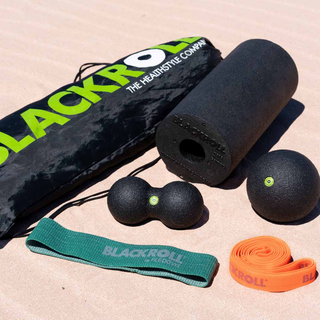 Blackroll fitness tools including a foam roller, massage ball, peanut ball and resistance bands on the sand.