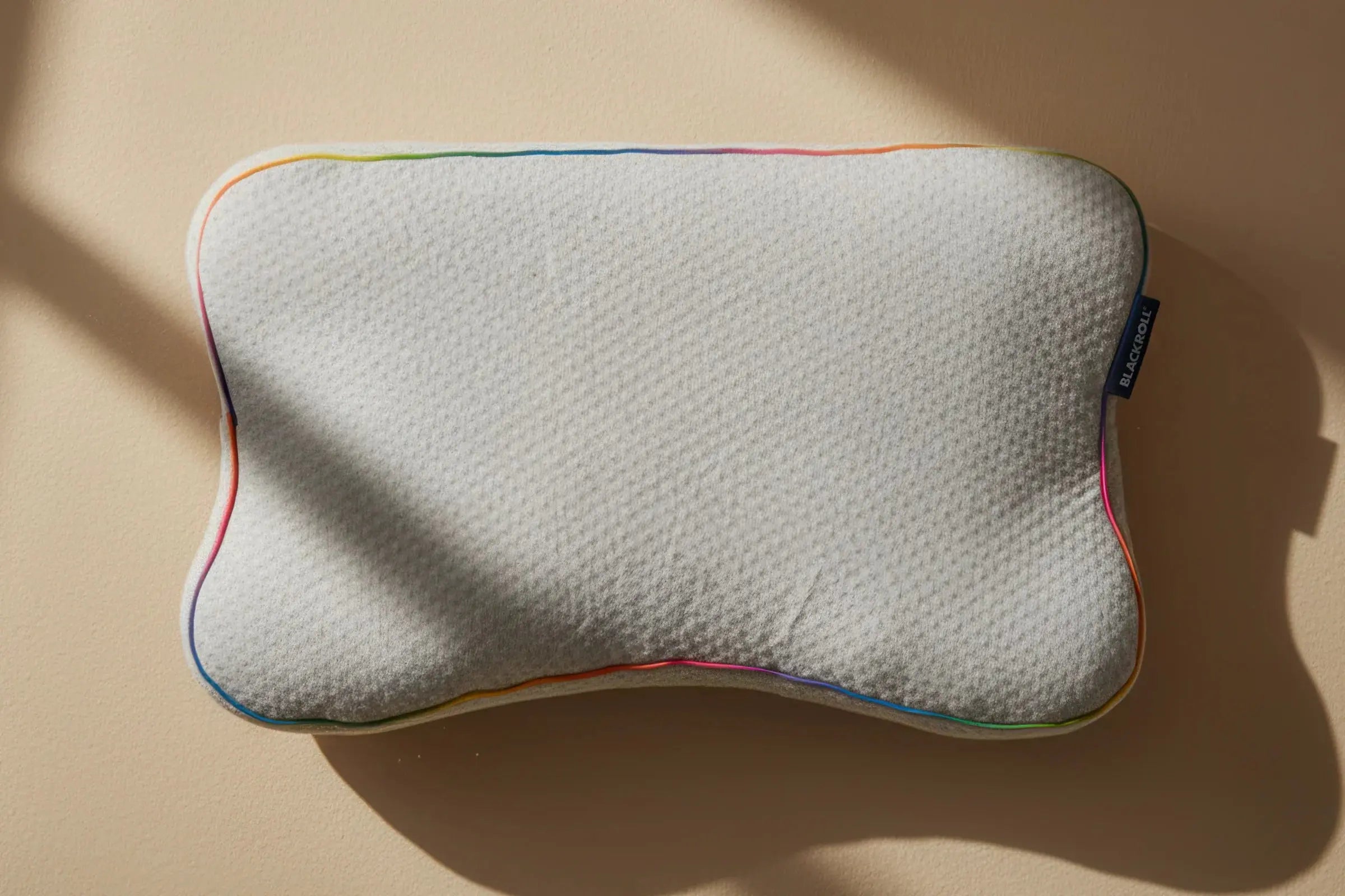 A kids size blackroll recovery memory foam pillow that is white with a rainbow border.