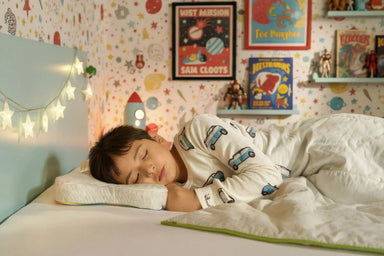 A child sleeping on their side in a bed on the Blackroll recovery kids pillow.