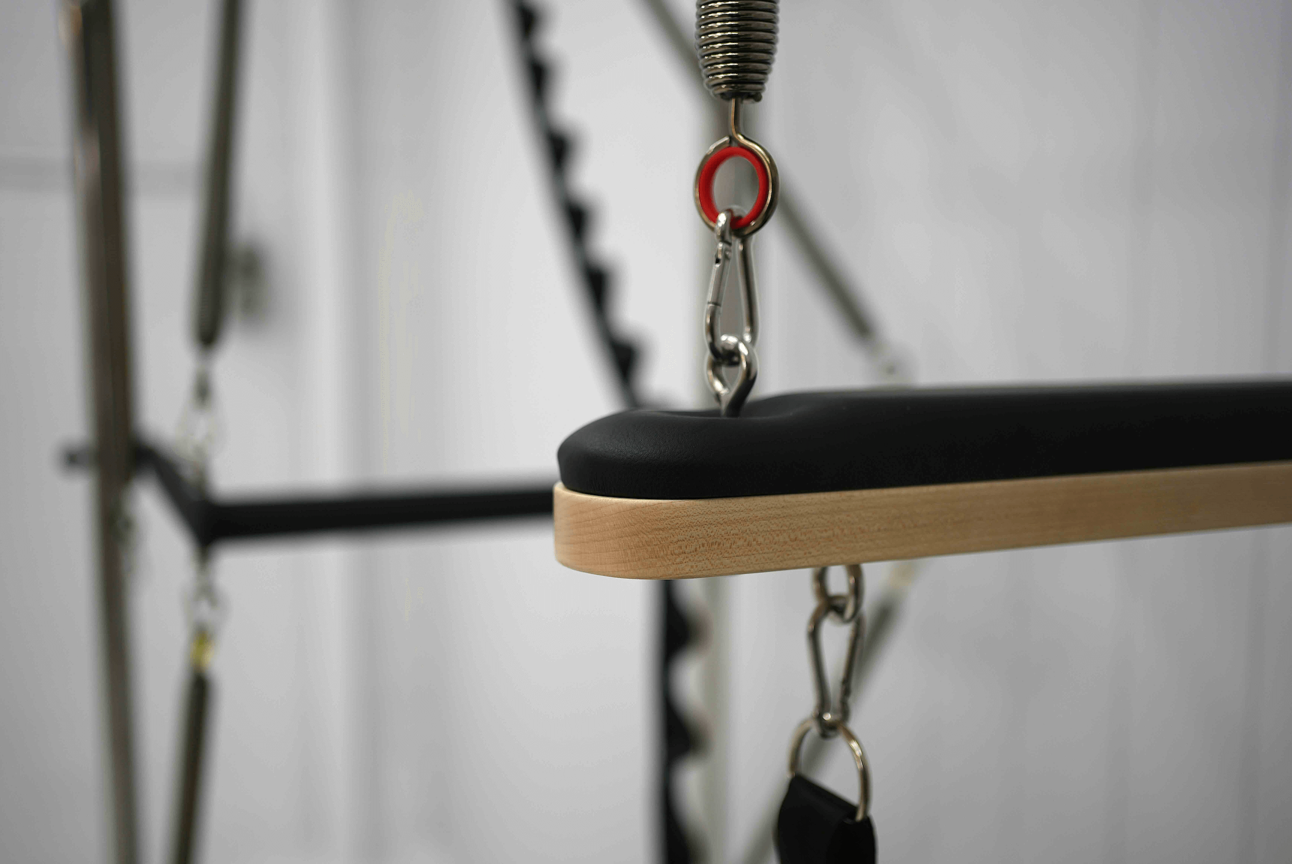 Close up of wooden bar attachment on queen reformer full trapeze with red spring showing.