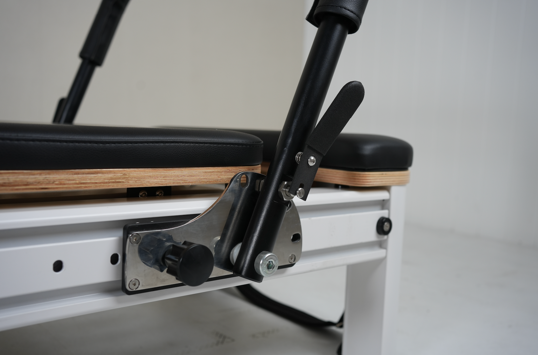 Close up of the foot bar adjuster of the Core Collab queen Pilates reformer with black upholstery and black footbar.