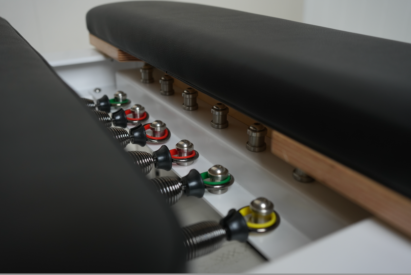 Close up view of the springs on the core Collab Queen Pilates reformer, showing 3 red springs, 2 green and 1 yellow.