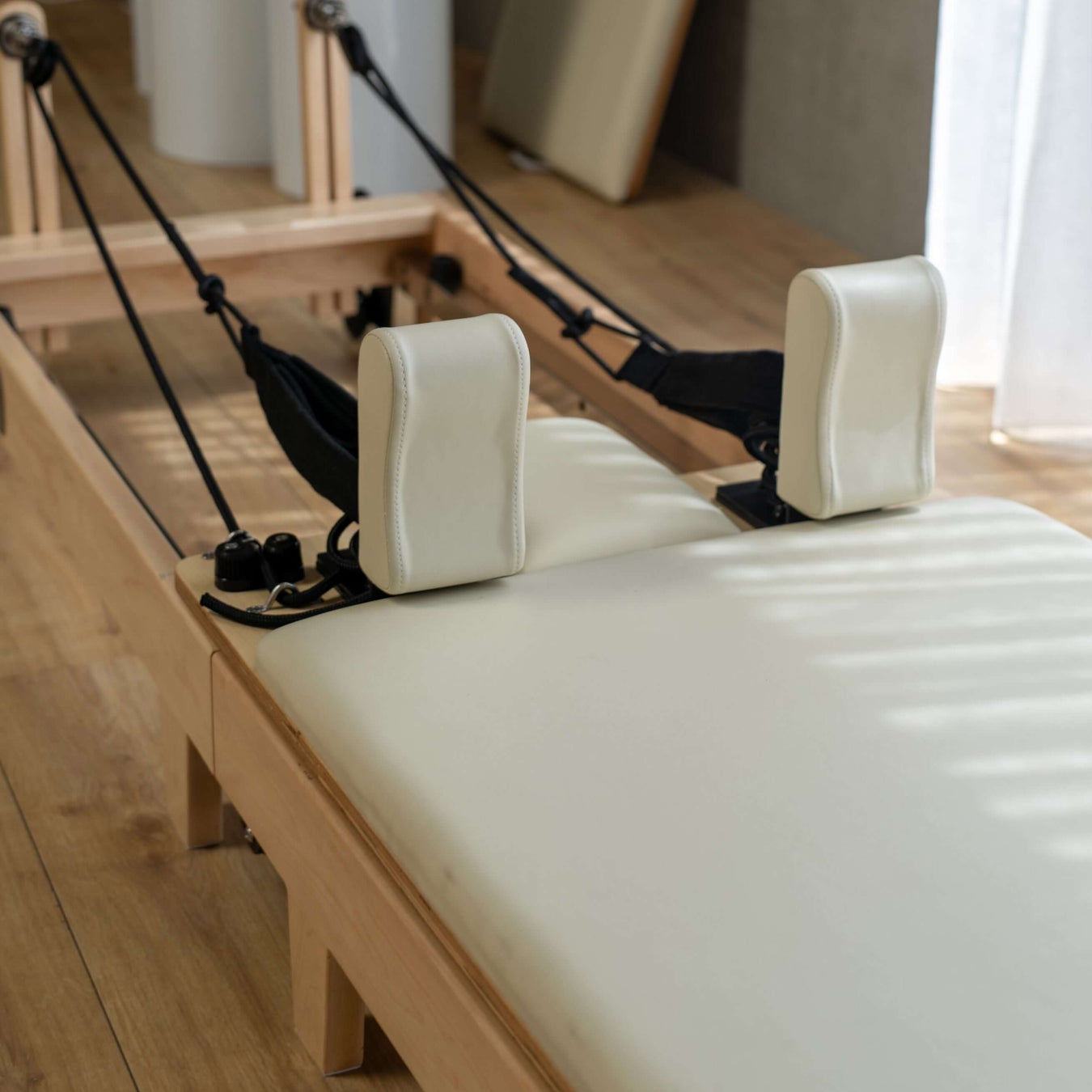 Close up of the carriage of a Core Collab Foldable Eco Pilates reformer with white upholstery in a home setting.