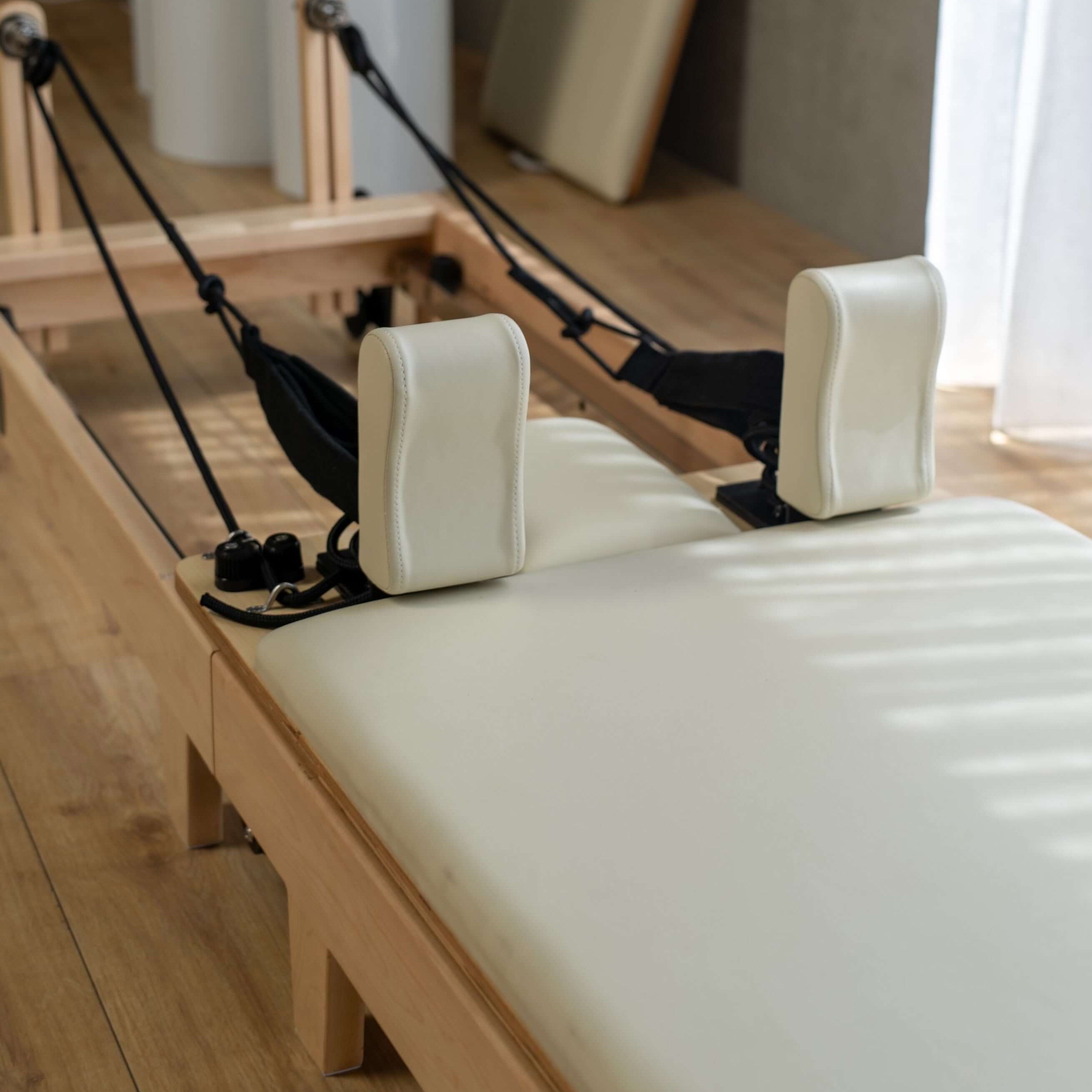 Close up of the carriage of a Core Collab Foldable Eco Pilates reformer with white upholstery in a home setting.