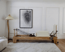 Core Collab Eco Pilates reformer in a living room setting, with view of the Beechwood frame and off-white upholstery from the side.