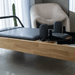 Close up of the Core Collab Eco Warrior Pilates Reformer showing a Beechwood frame and charcoal upholstery in a room with a cream coloured chair.