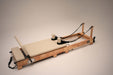 Angle view of the Core Collab Foldable Eco Pilates Reformer in beige, on a beige background.