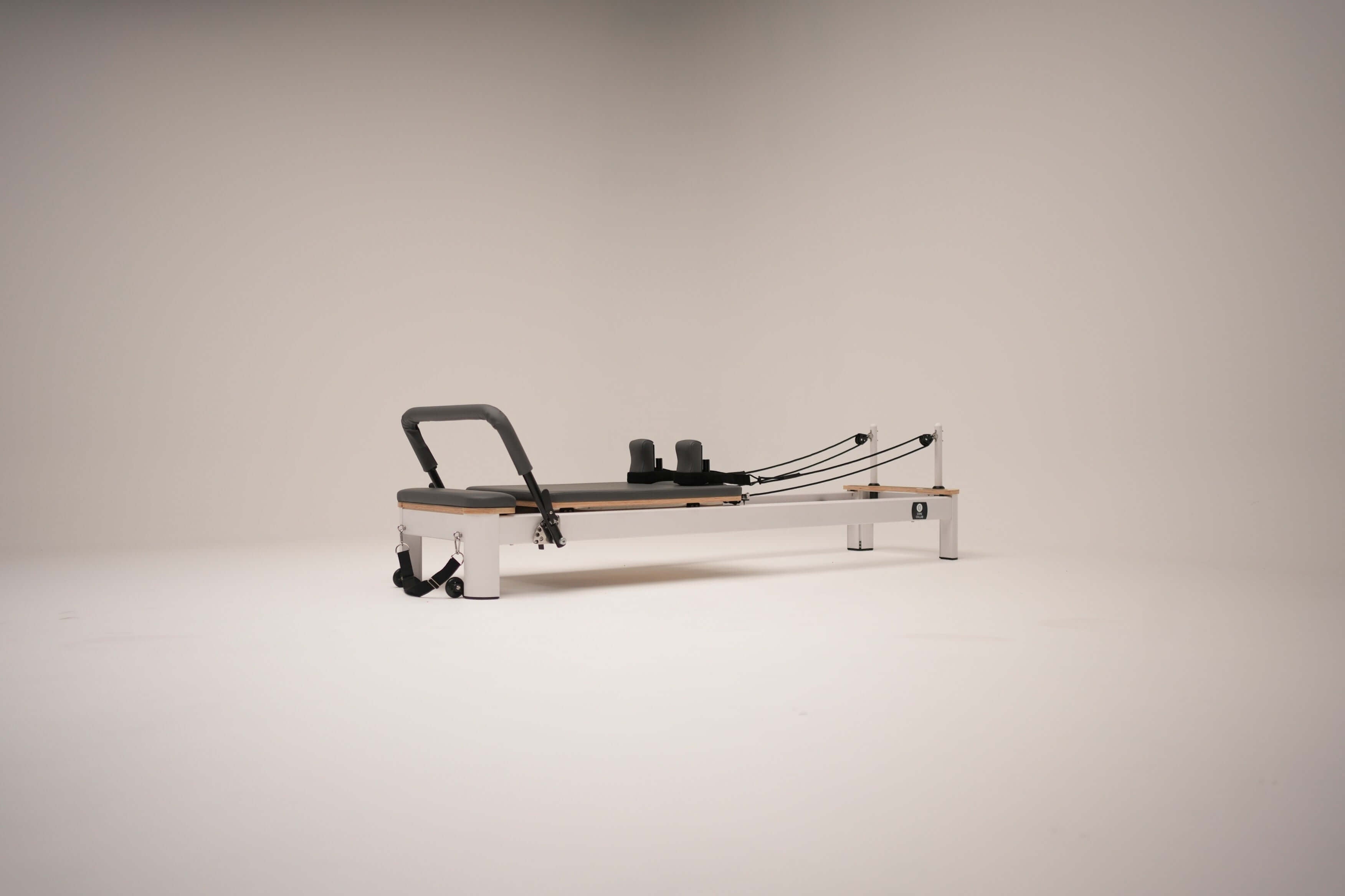 The Core Collab Queen studio reformer with white frame with charcoal upholstery on a white background.