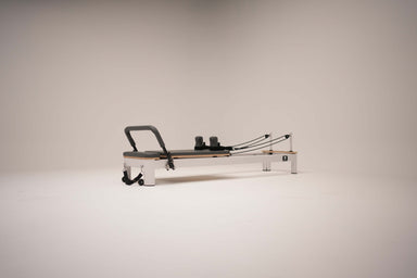 The Core Collab Queen studio reformer with white frame with charcoal upholstery on a white background.