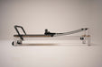 Side view of the Core Collab Queen Studio Pilates reformer showing the white metal frame with charcoal upholstery.