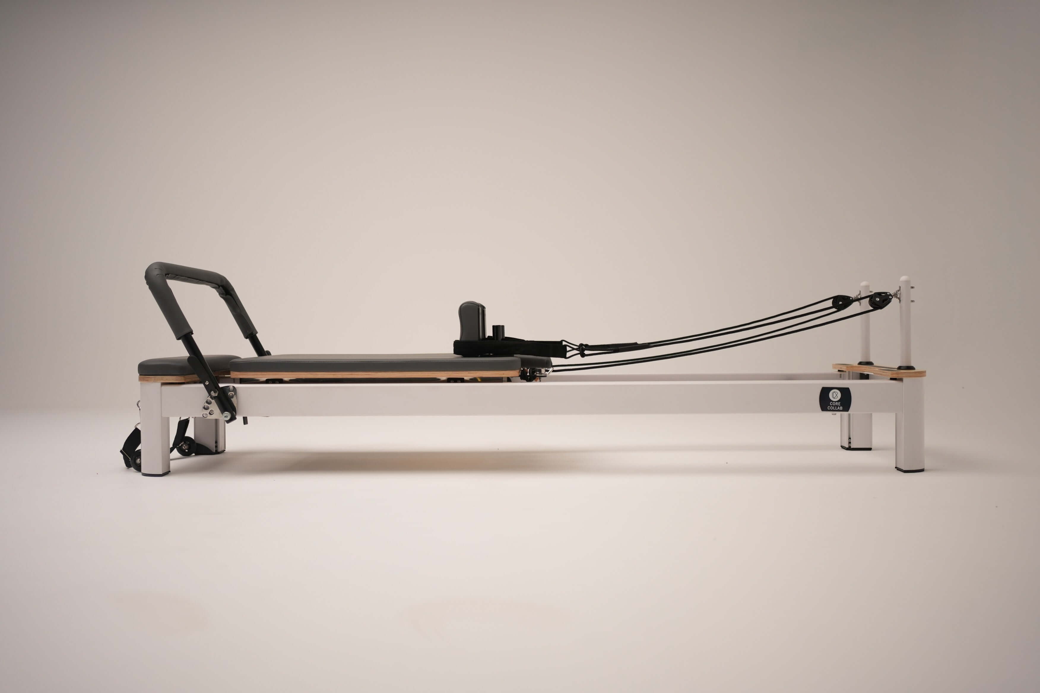 Side view of the Core Collab Queen Studio Pilates reformer showing the white metal frame with charcoal upholstery.