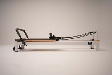 Side view of the Core Collab Queen Studio Pilates reformer showing the white metal frame with charcoal upholstery.