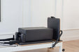Core Collab Queen Studio Pilates reformer with the sitting box and jumpboard attached, in charcoal upholstery with a white frame.