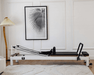 Core Collab Queen Studio Pilates reformer in a living room setting, with white frame and black upholstery.
