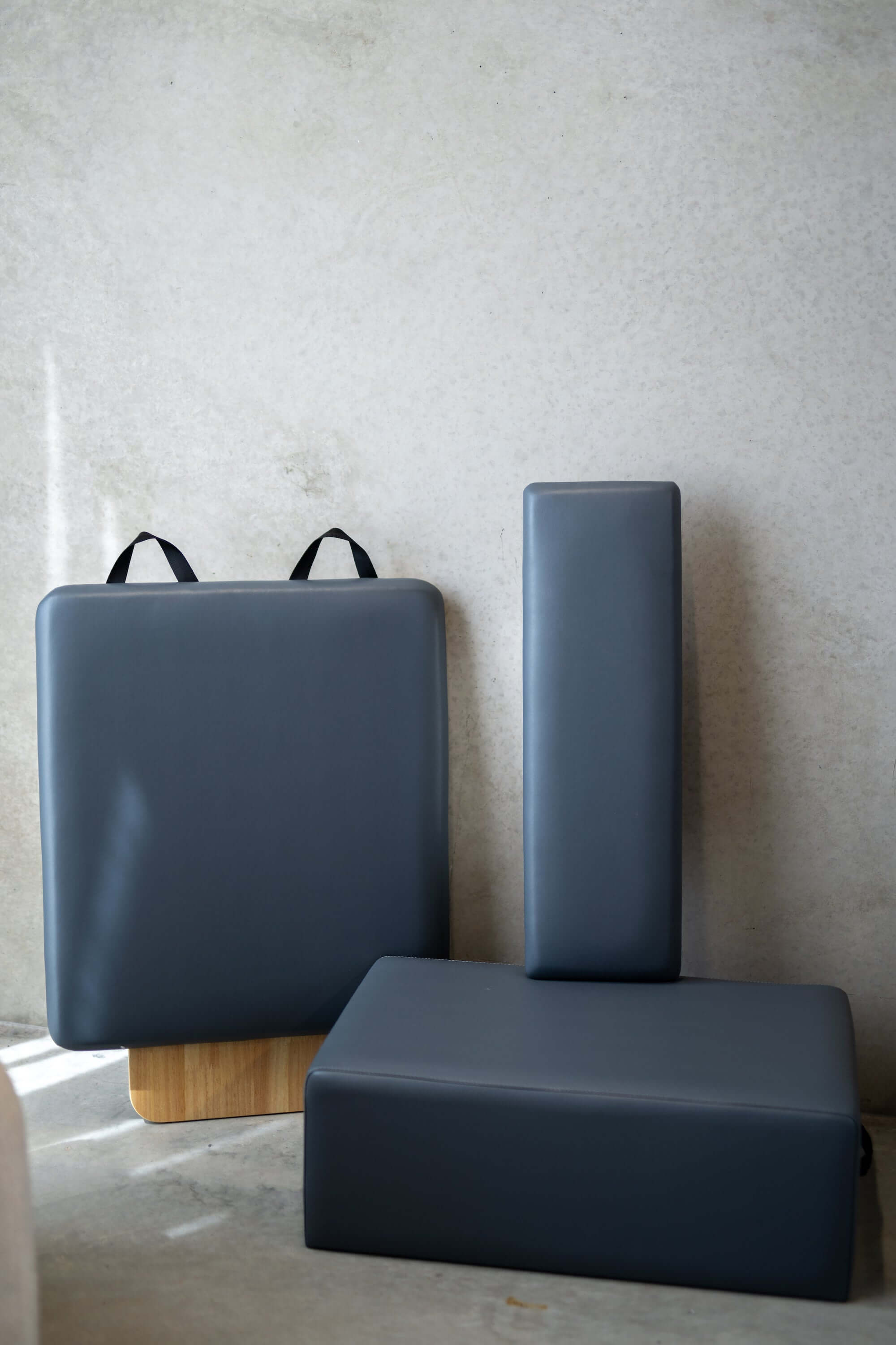 The accessories included with the Core Collab Queen Studio Pilates reformer, showing the jumpboard, sitting box and platform cushion in charcoal.