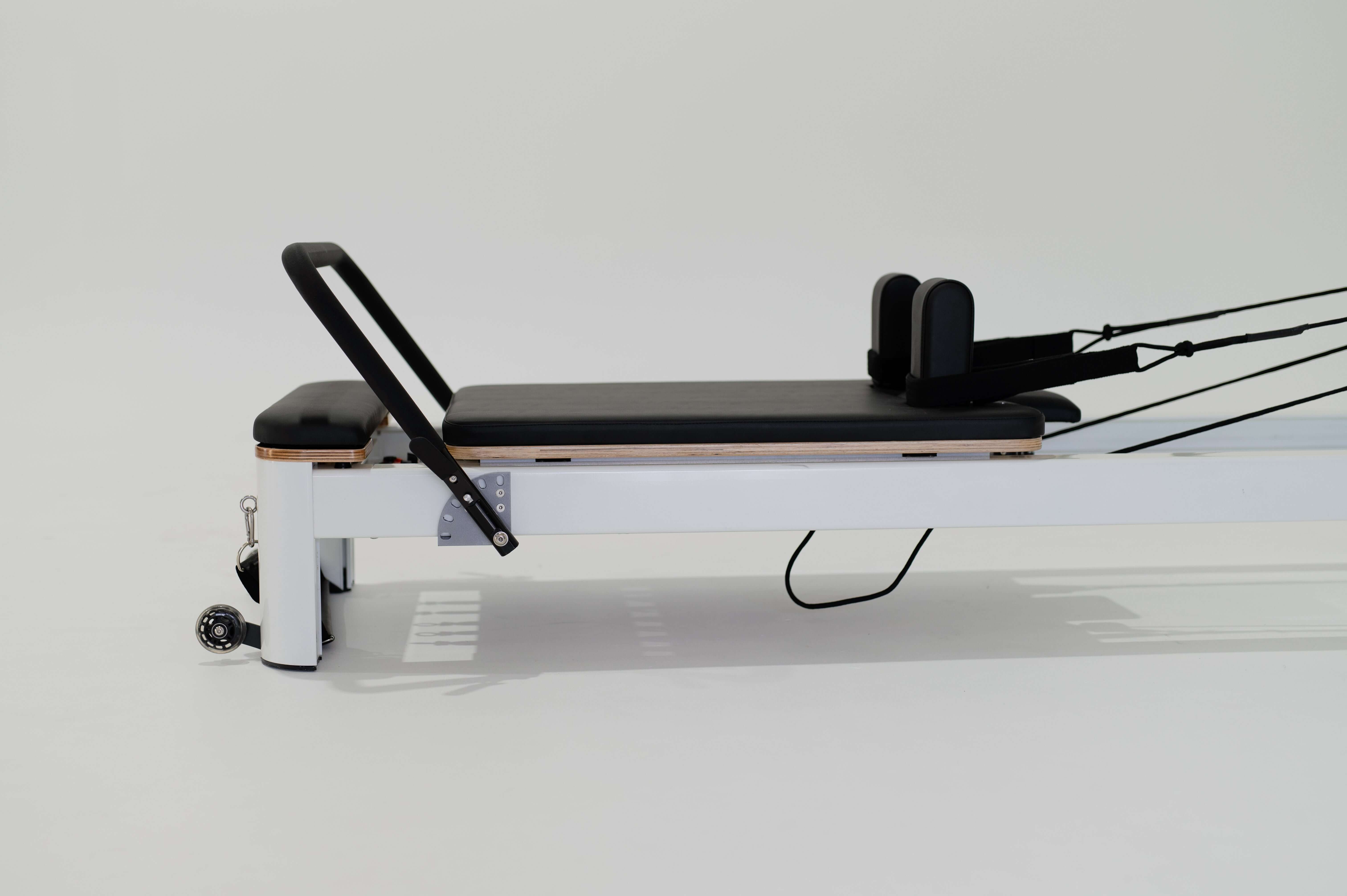 Core Collab Queen Studio Pilates reformer side view of the top half showing the white frame with black upholstery, with the footbar and shoulder rests in view.