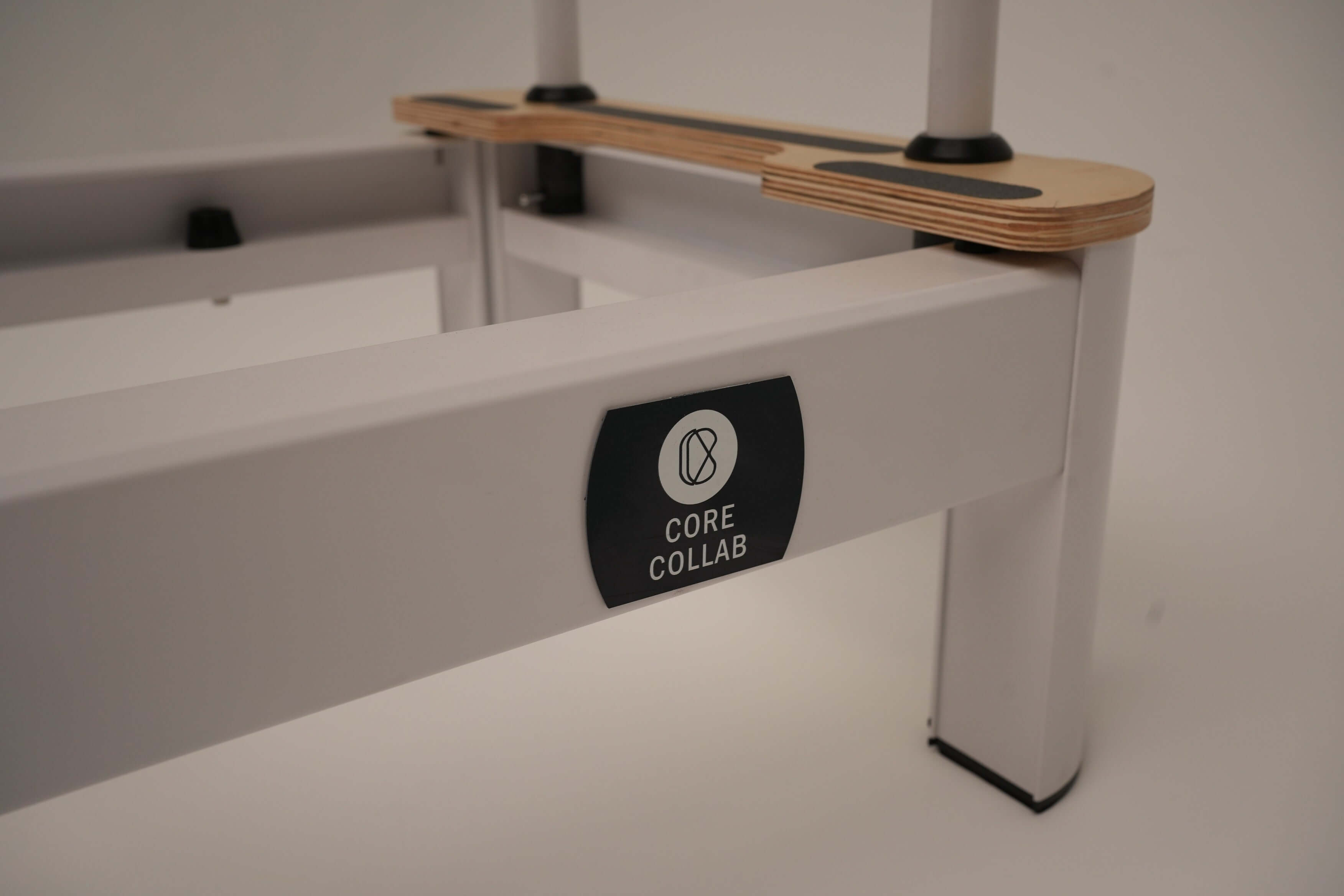 close up of the core Collab Queen Studio Pilates reformer showing the black core collab logo plate on the white frame.