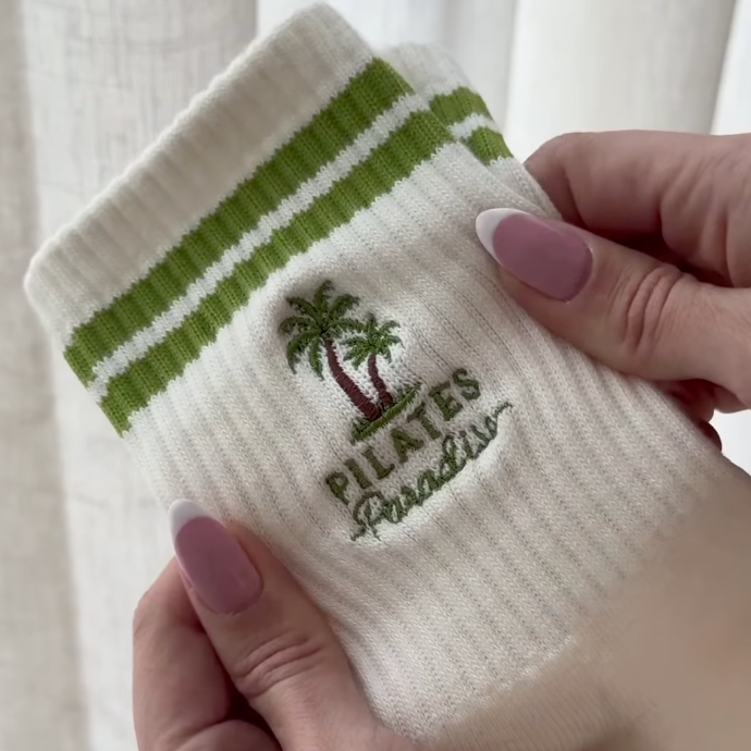 Close up of Elliosa Pilates Paradise grip socks showing the embroidered palm trees and text, with two green stripes at the ankle