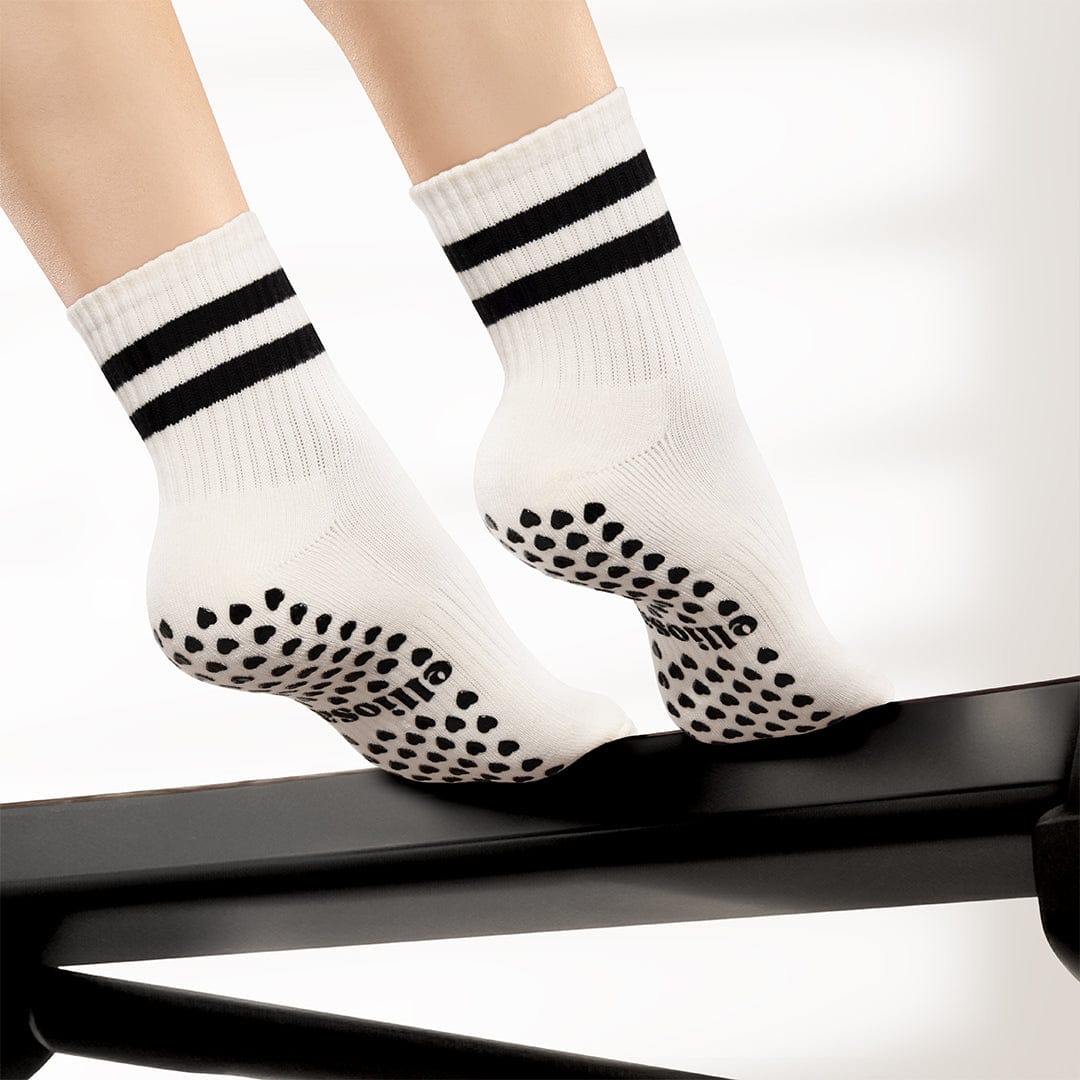 Person wearing Elliosa dual direction grip socks in coconut cream, using a Pilates reformer.