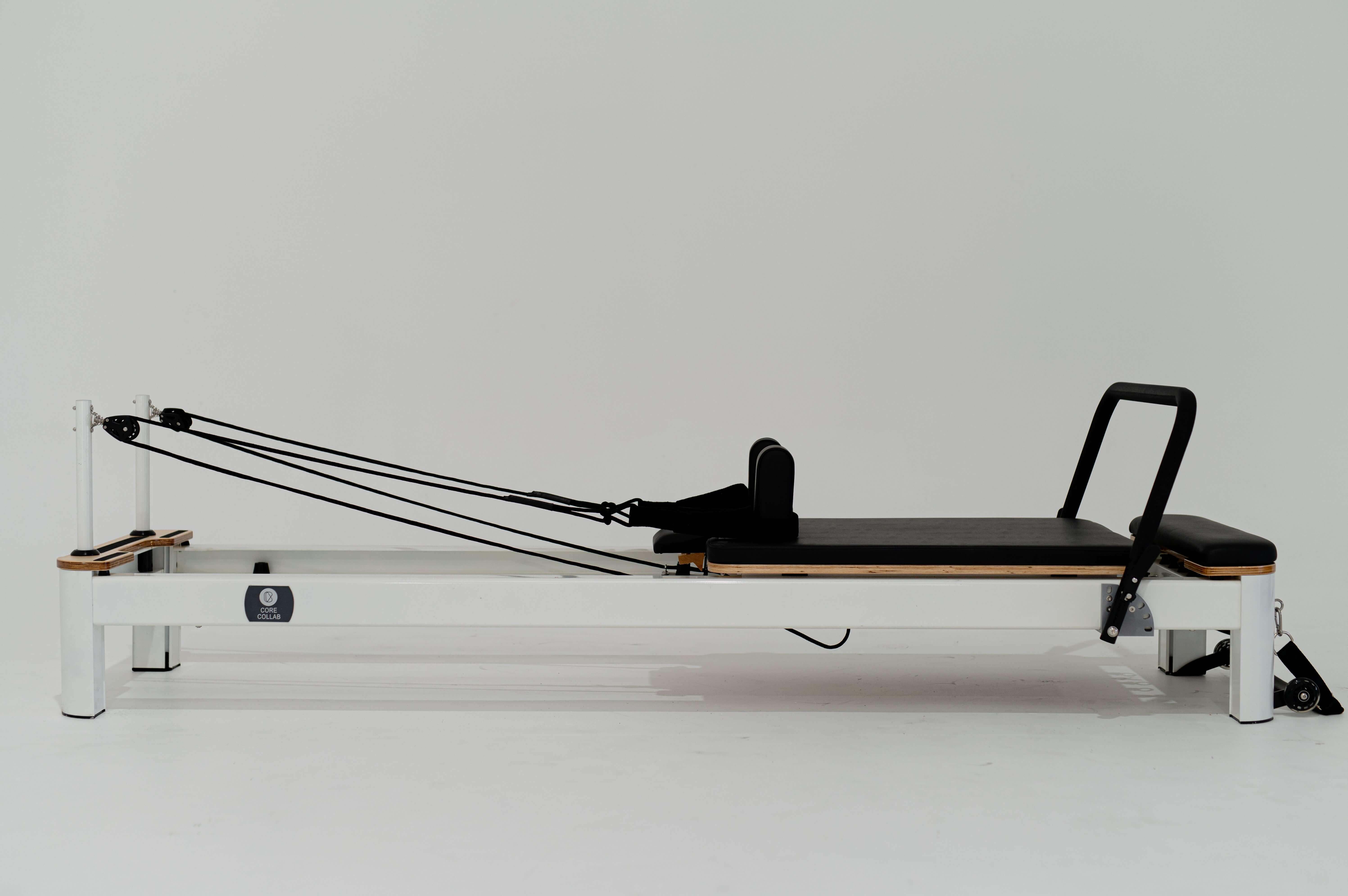 Core Collab Queen Studio Pilates reformer full side view showing white frame and black upholster on a white background.