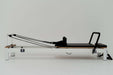 Core Collab Queen Studio Pilates reformer full side view showing white frame and black upholster on a white background.
