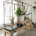 Full trapeze reformer in a studio setting with greenery in front of window with sheer white curtains.